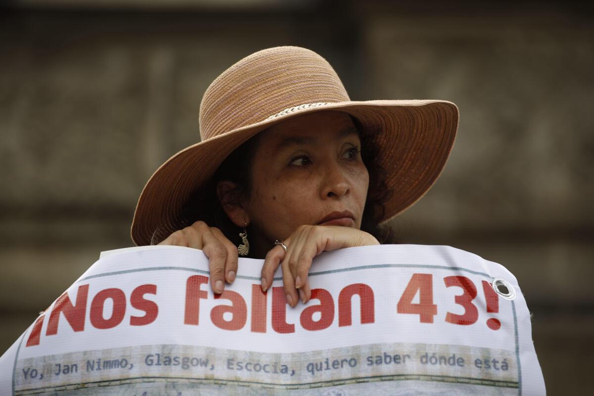 A woman in a wide-brimmed hat carrying a sign that reads "We are missing 43!" in Spanish. 