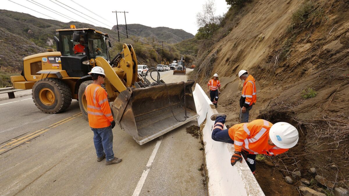 A Cal Trans crew works to place temporary concrete walls (K-rails) on Topanga Canyon Boulevard Monday after large rocks, dirt and debris likely loosened by last week's rainstorm fell onto the pavement, temporarily shutting down the roadway.
