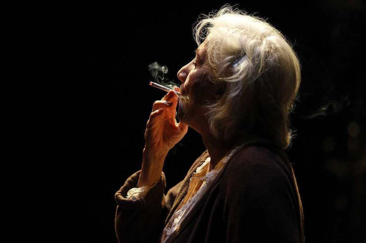 Olympia Dukakis is seen in profile in dark light, smoking a cigarette