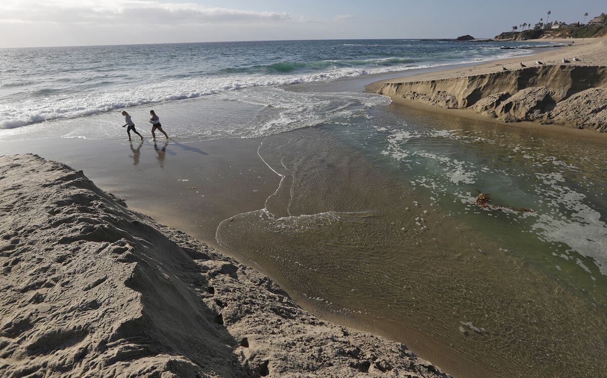 Beachgoers walk along Aliso Beach past the Aliso Creek where it meets the ocean.