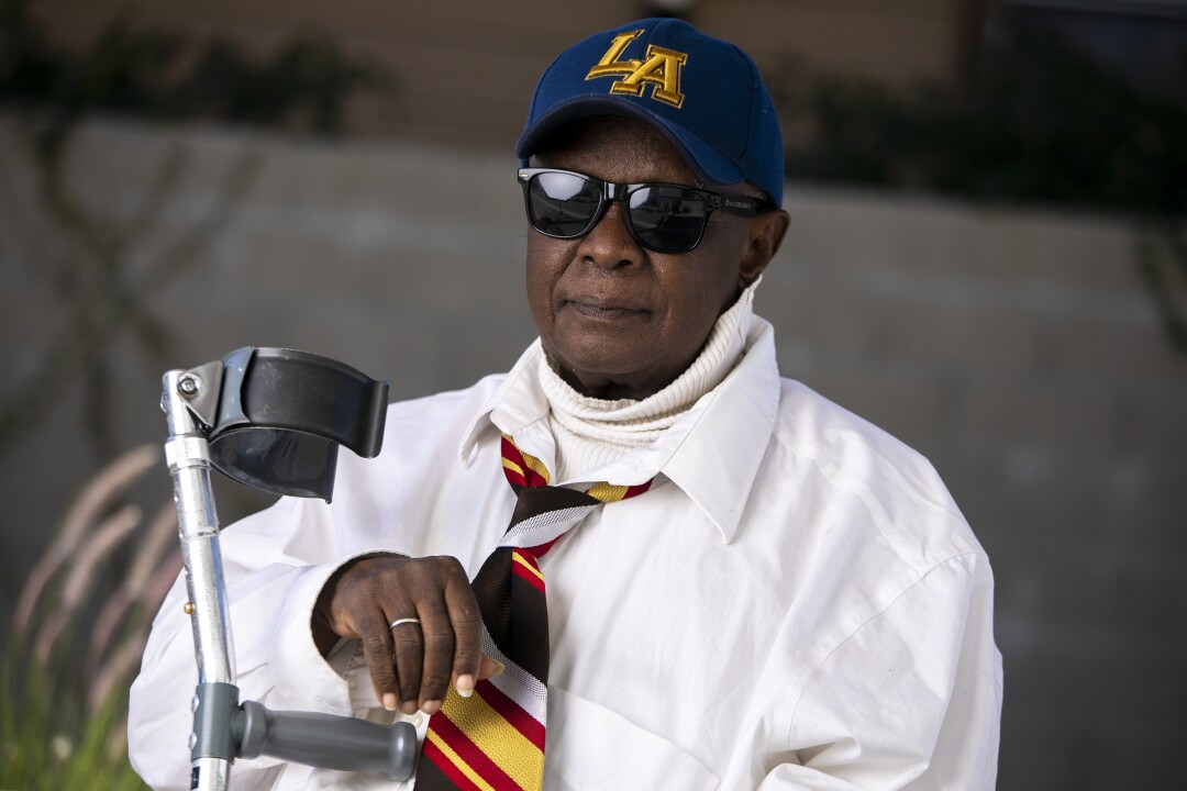 Eddie Johns in a white shirt and colorful tie, with a crutch.
