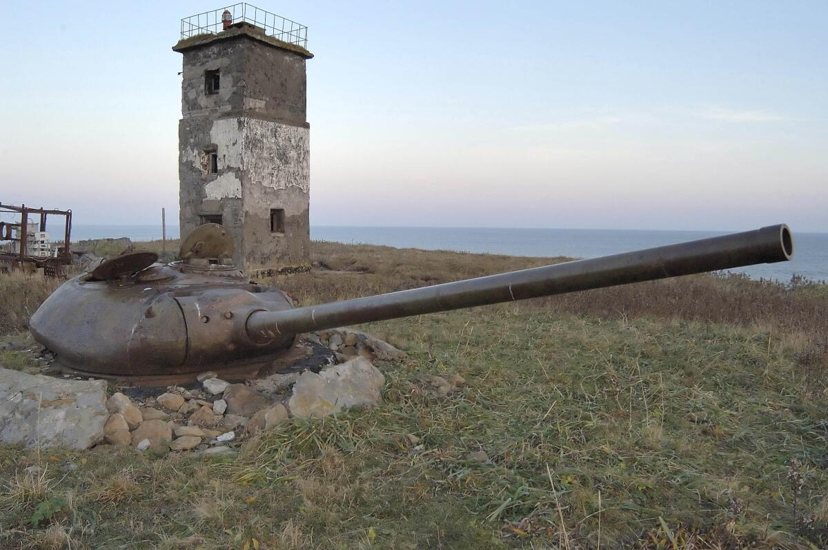 A turret from an old tank set in the ground in front of a lighthouse on Kunashiri Island.