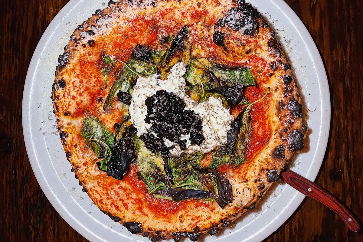 An overhead photo of a Margherita pizza topped with burrata, atop which is caviar.