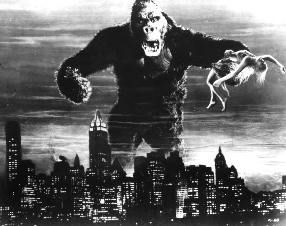 A giant ape holding a woman in one mighty paw looms over the Manhattan skyline.