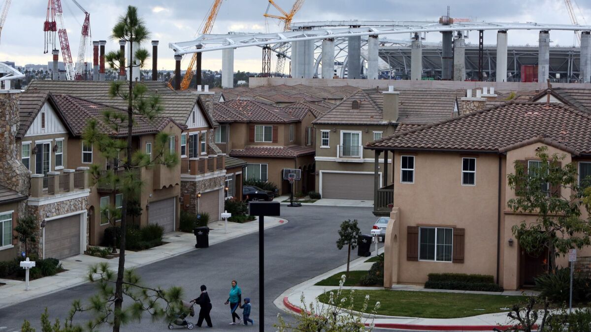 People cross the street in the Renaissance Homes, a gated community covering 37 acres in Inglewood, Calif. on February 20. Construction of the Rams-Chargers Complex is seen in the background.