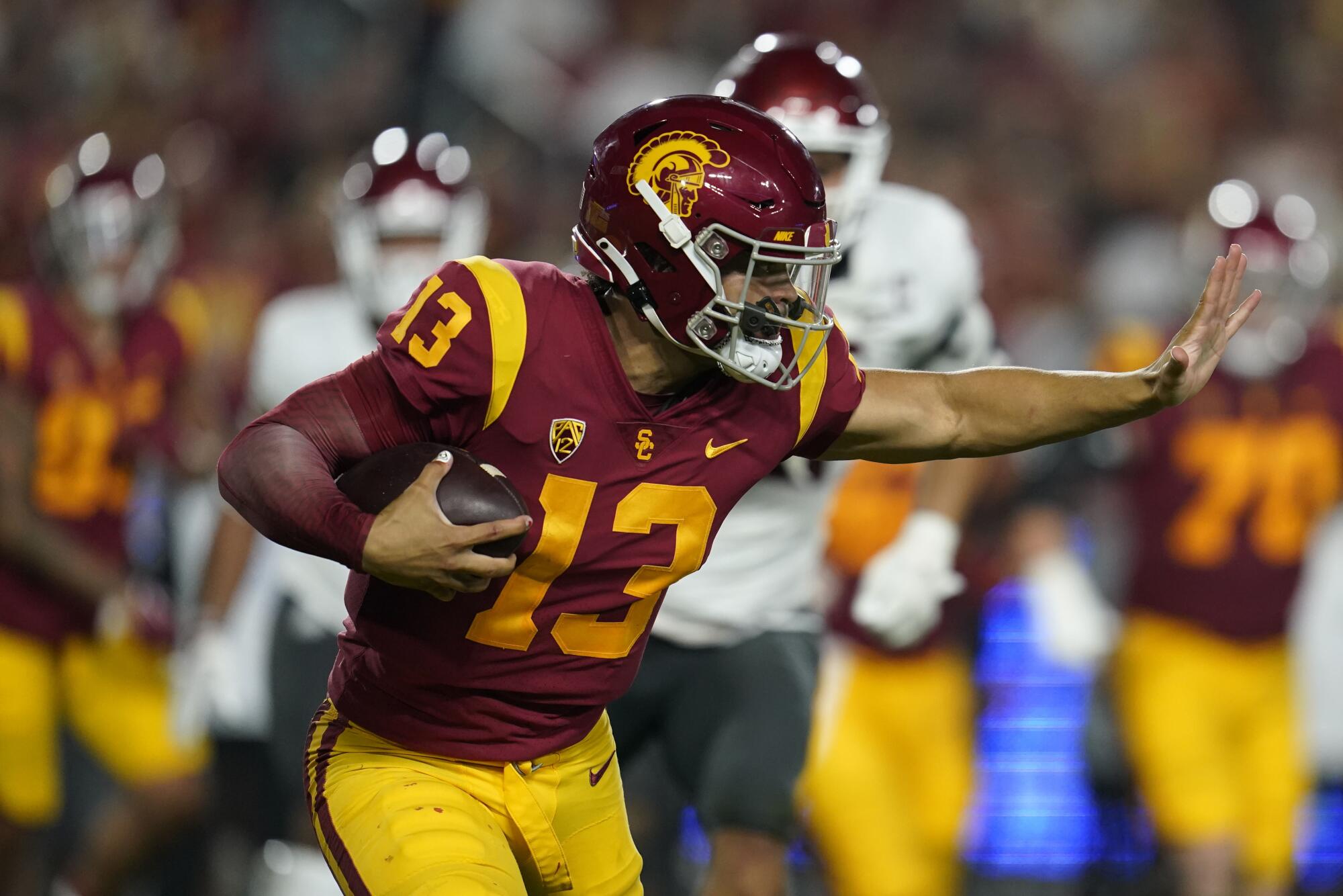 USC quarterback Caleb Williams thrusts his arm out to avoid a tackle while carrying the football
