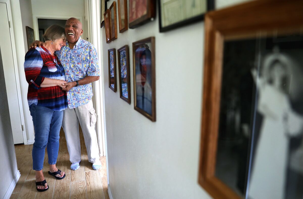 Charles and Janice Tyler are photographed in a hallway lined with family photographs including their wedding day photo, at right, at their Huntington Beach home.