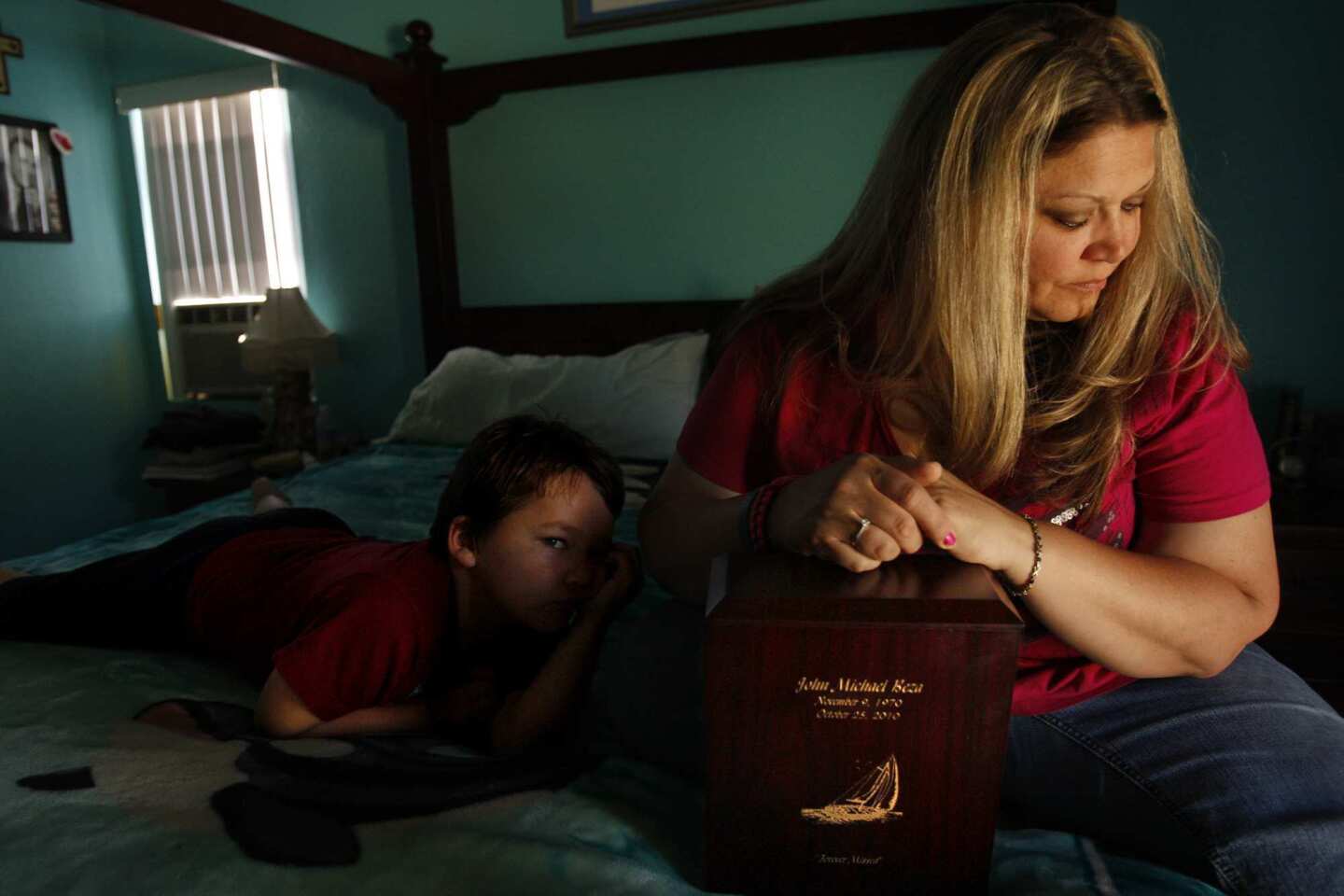 Megan Beza, with son Jacob, 5, leans on the wood box that holds her husband John's ashes. The box is carved with a picture of the sailboat they long talked about buying. John committed suicide in 2010.