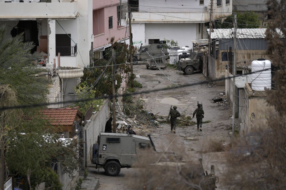 A wide overhead shot of two soldiers walking between buildings in a refugee camp.
