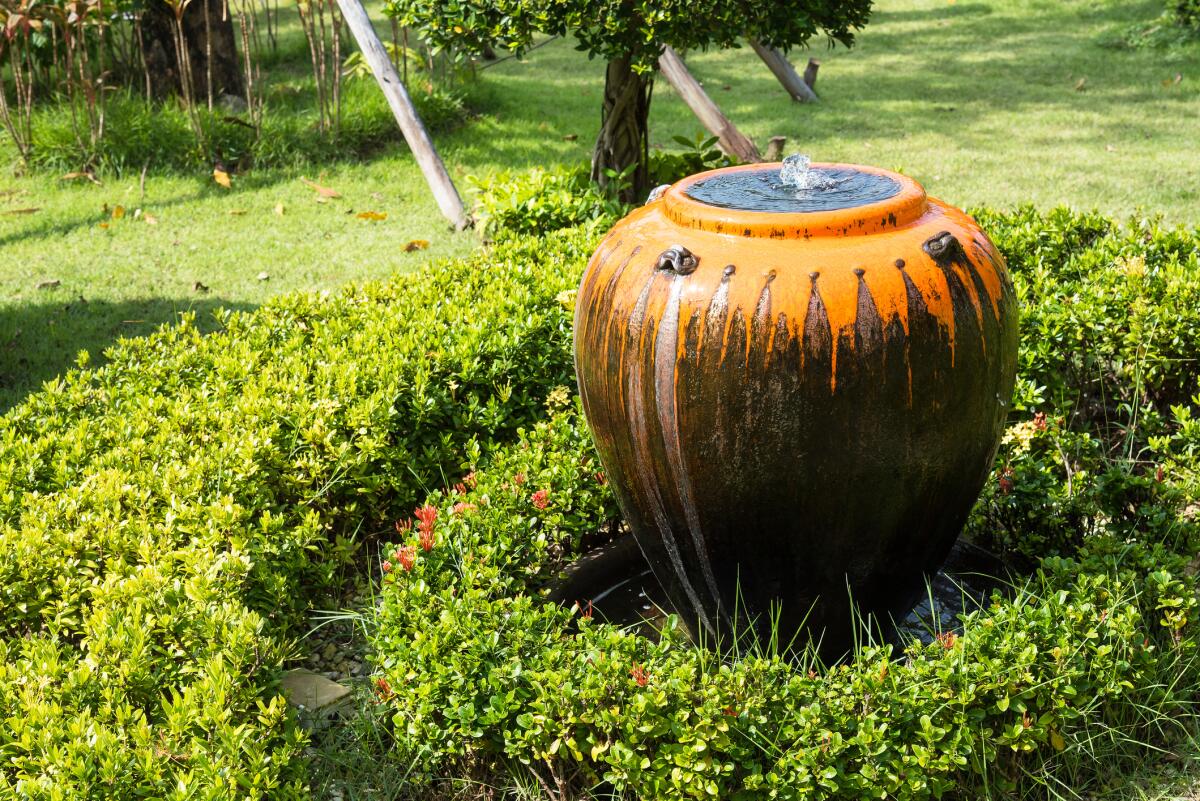 A large ceramic jar serves as a bubbling water fountain in a green garden.