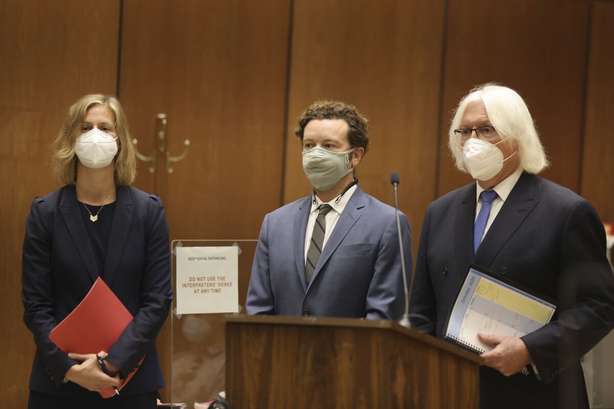 A defendant stands with lawyers in a courtroom.
