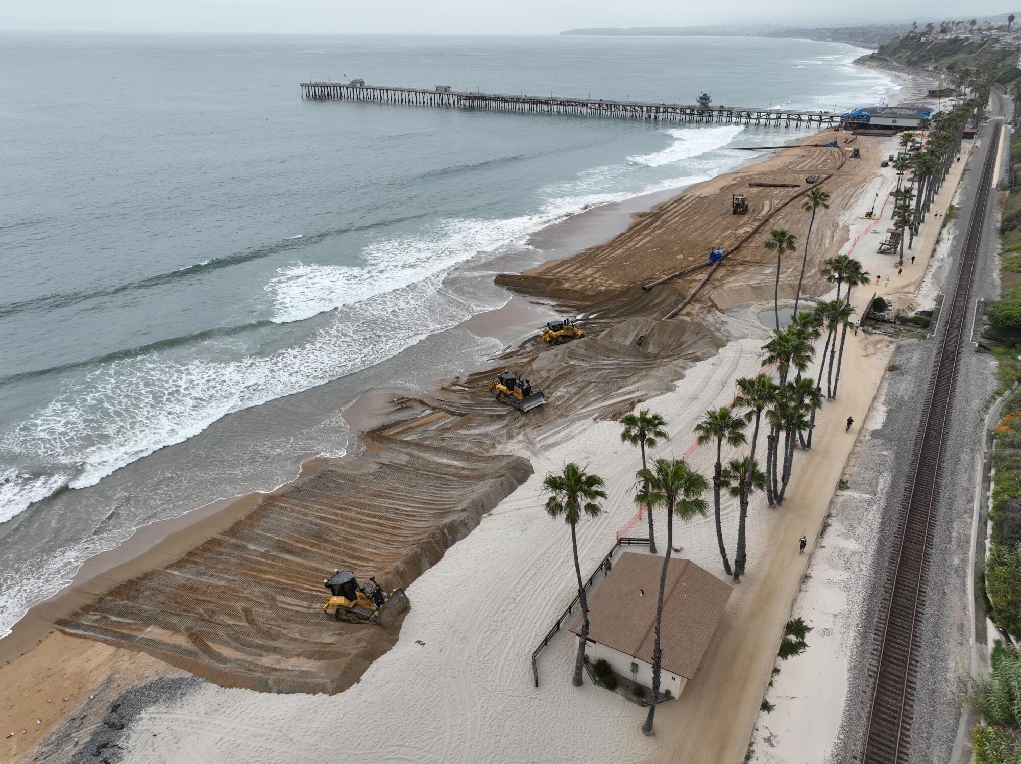 Workers replenish the beach with new sand south of the pier in San Clemente.