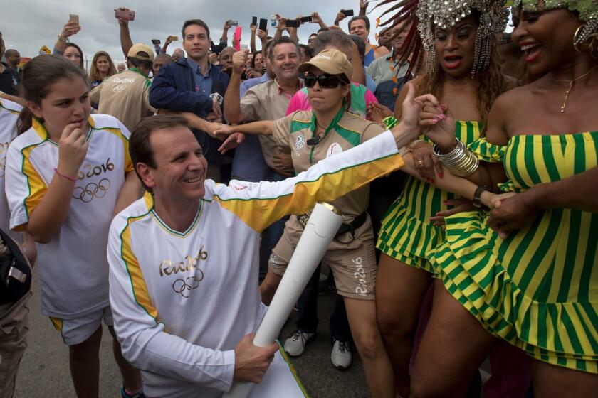 File - In this Aug. 3, 2016 file photo, Rio de Janeiro's Mayor Eduardo Paes, center, holds the Olympic torch, while members of the Mangueira samba school dance, in Rio de Janeiro, Brazil. The former Rio de Janeiro Mayor, the moving force behind organizing last year's Olympics, is being investigated for accepting at least 15 million Brazil reals ($5 million) in payments to facilitate construction projects tied to the Games. (AP Photo/Silvia Izquierdo, File)