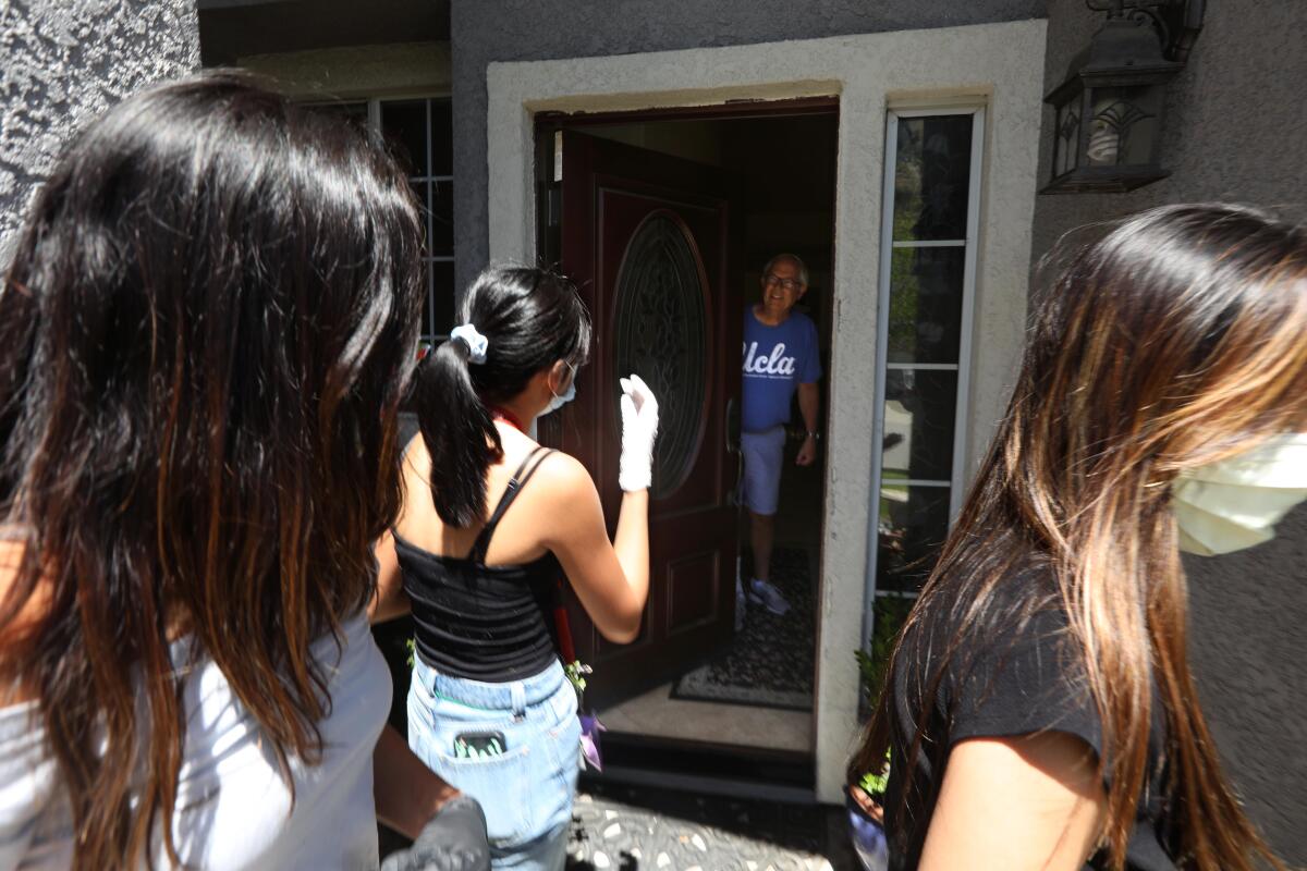 Sharia Busnawi, 16, from left, Christine Riel, 16, Krysta Mendoza, 17, juniors at West Ranch High School, deliver a grocery order to Randy Gilpin, 67, in Saugus on Tuesday for Six Feet Supplies, a volunteer service that shops for homebound people.