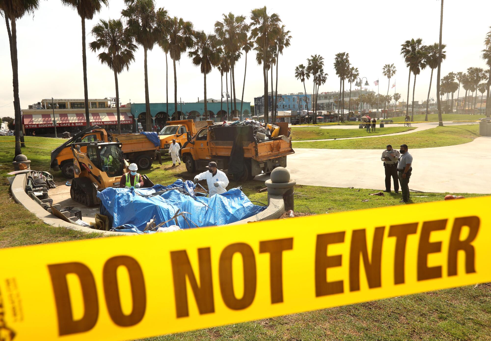 Yellow tape surrounds a scene as workers clean up a homeless encampment