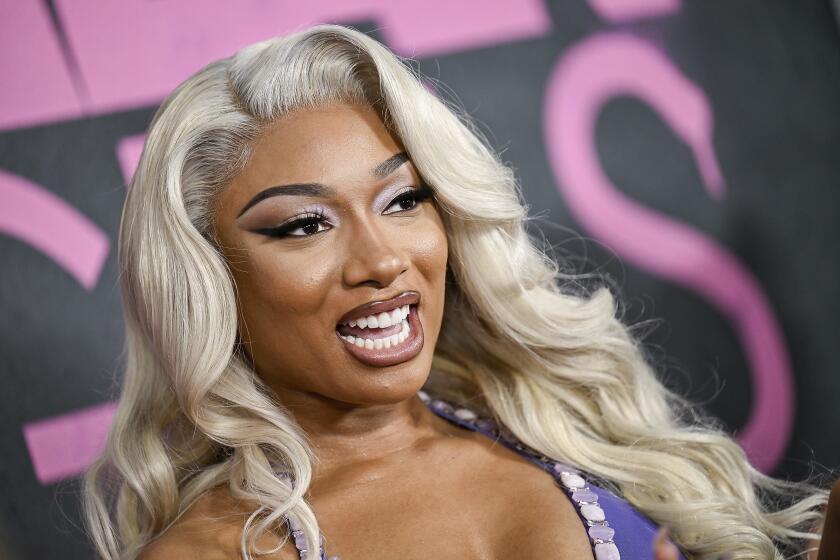 An angled image of Megan Thee Stallion smiling with an open mouth while clad in a purple halter dress with long platinum hair