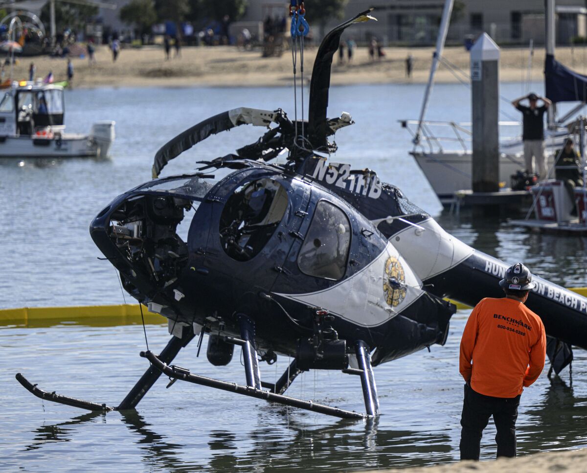 A crane lifts a mangled helicopter out of the water as a worker watches