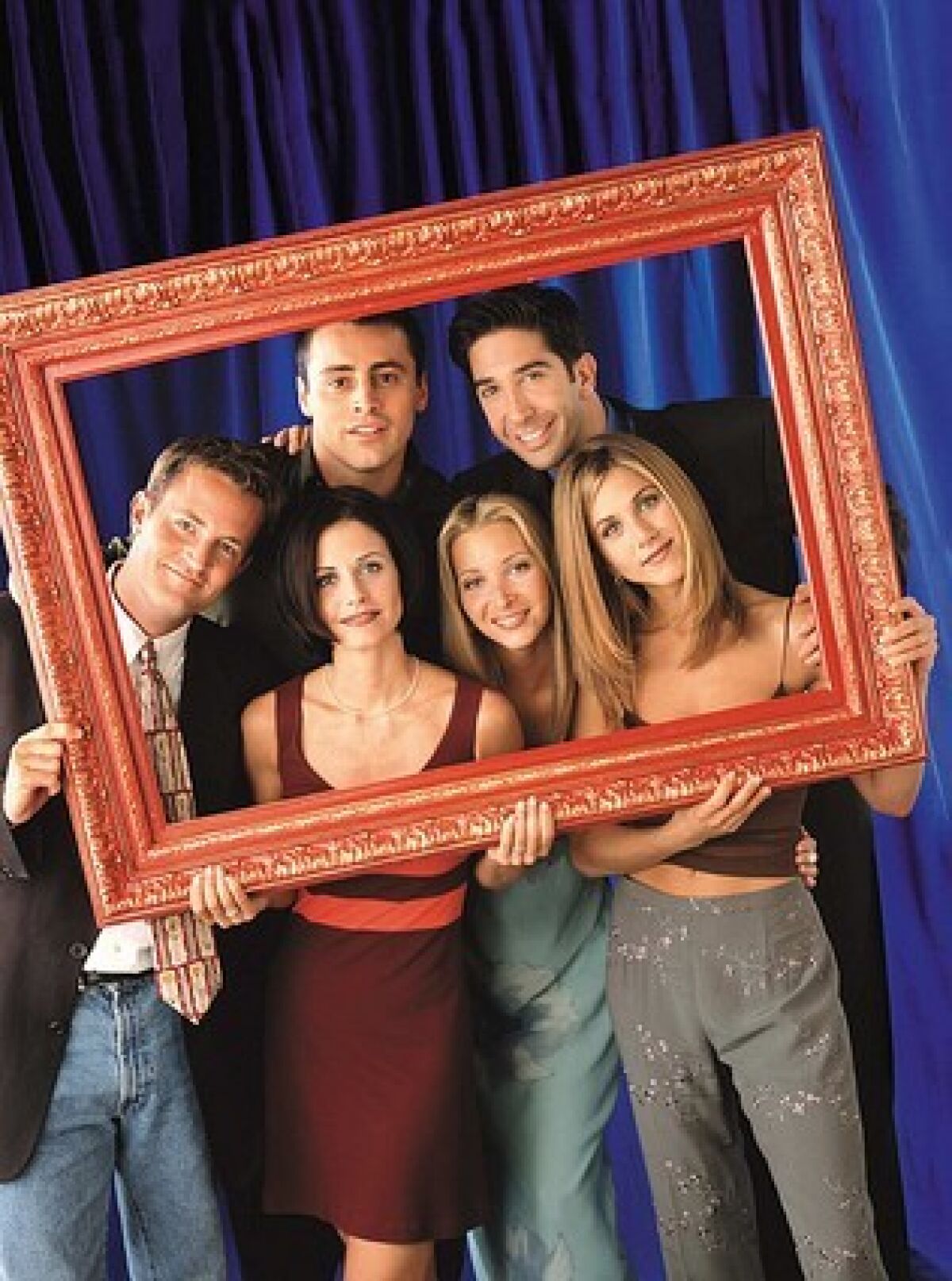 The cast of "Friends" holding a large photo frame around themselves.