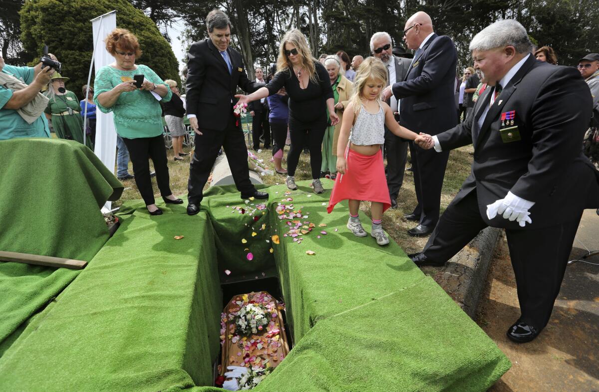 Mourners including Lillet Gustavson, 6, toss rose petals on the lowered casket of “Miranda Eve” during a graveside service in Colma, Calif., in June.