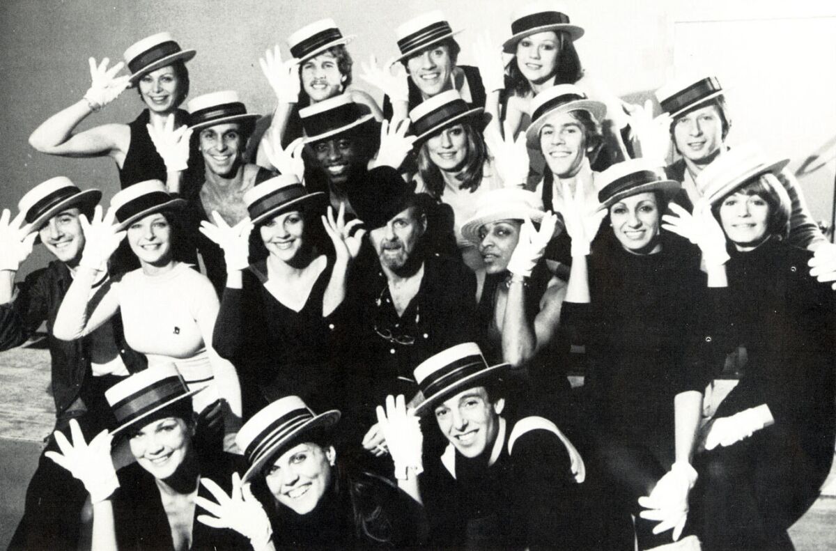 A black and white photo of a large group of people tipping their hats 