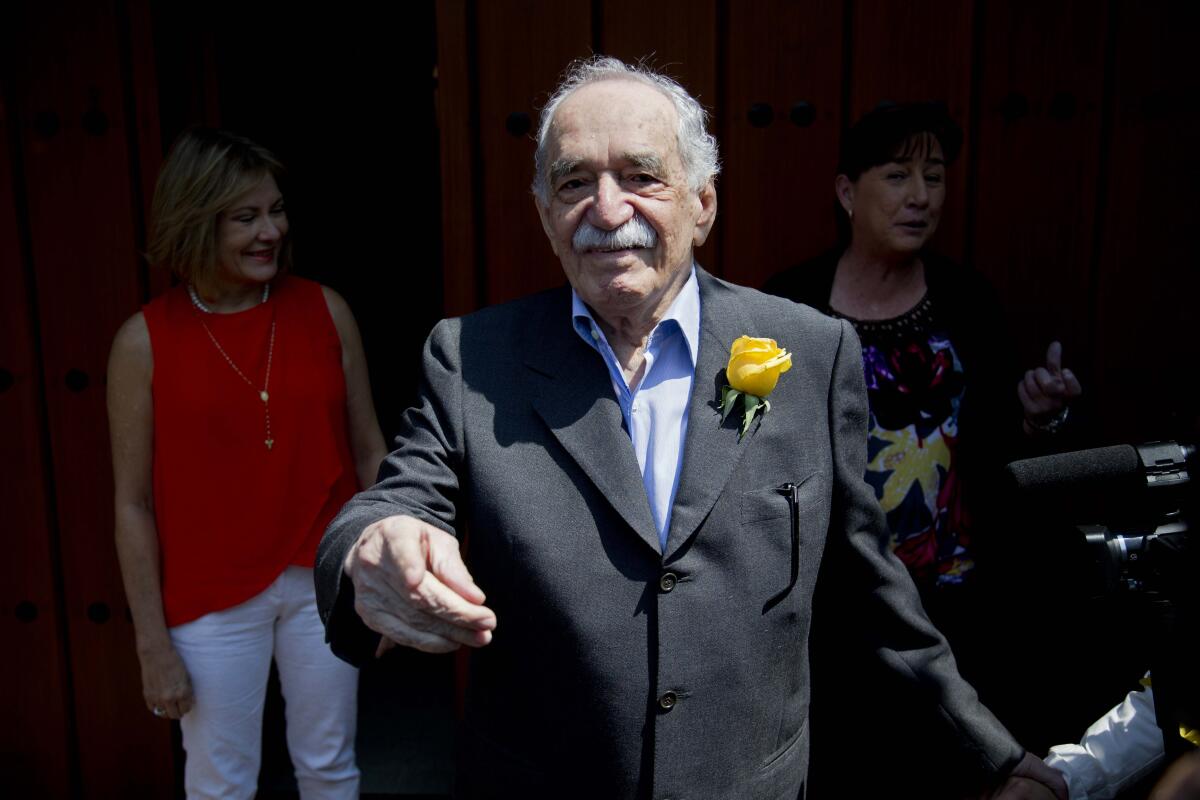 Gabriel Garcia Marquez, in a blue suit jacked and a yellow rose in his lapel, smiles and gestures at the camera