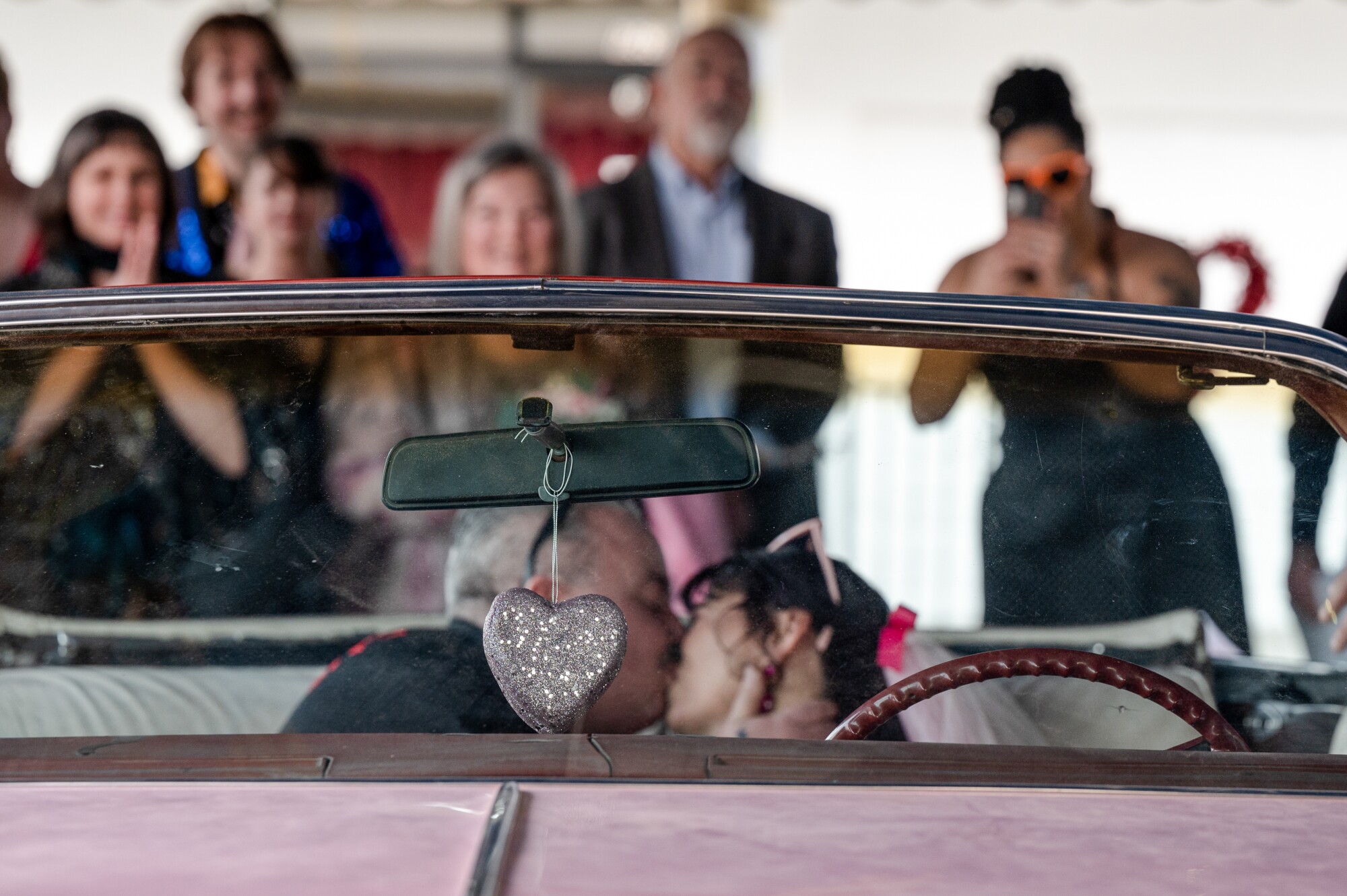 Two people kiss, sitting in the front seat of a vintage car