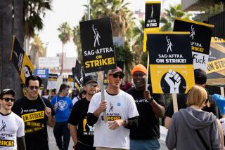 A large group of demonstrators walking and carrying picket signs that read, "SAG-AFTRA on Strike!"