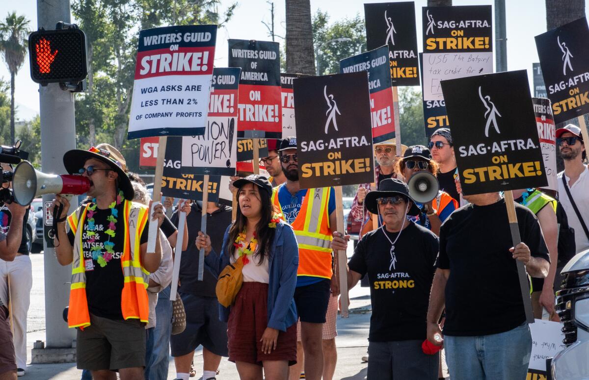 Strikers carry signs as they walk a picket line.