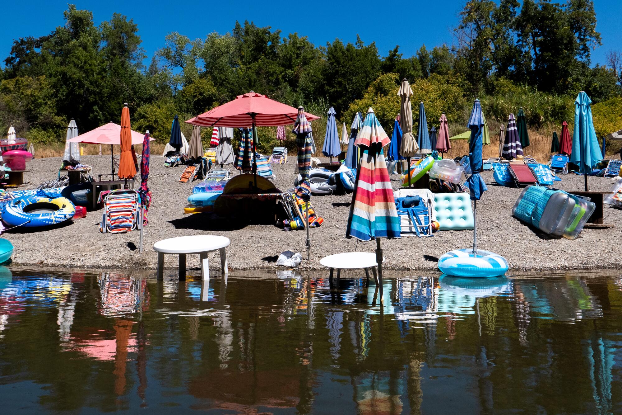 Colorful umbrellas and flotation devices crowd a Russian River beach. 