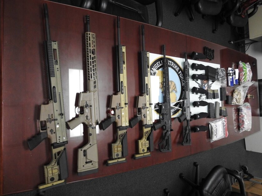 Six rifles, scopes, magazines, and bags and boxes of ammo laid out on a table