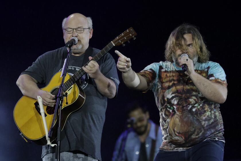 Kyle Gass closes his eyes while playing guitar and Jack Black points while singing next to him