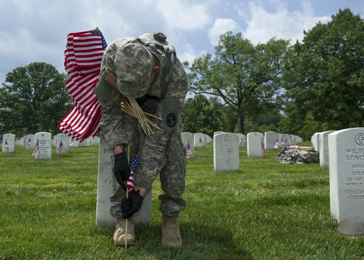 A soldier places flags at grave sites at Arlington National Cemetery in Va. as part of the annual "Flags-In" ceremony in preparation for Memorial Day.