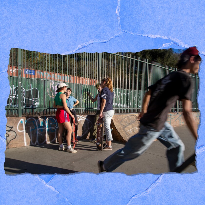 Young men and women skate and stand and talk at a skate park.