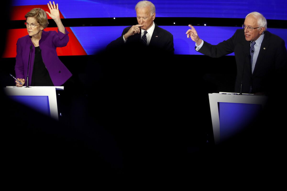 On Jan. 14, 2020, Sen. Elizabeth Warren and Sen. Bernie Sanders raise their hands to answer a question as Joe Biden pauses.