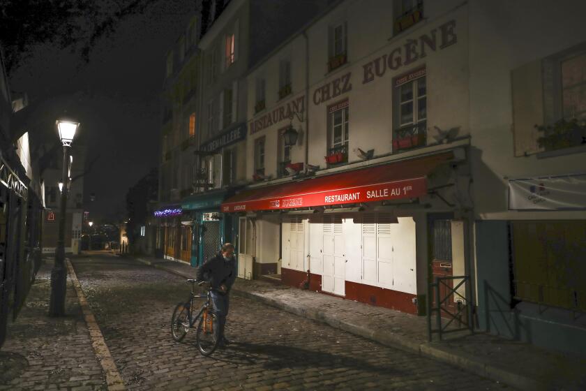 FILE - In this Dec. 15, 2020 file photo, a man pushes his bicycle along a row of closed restaurants in Montmartre, during the new imposed curfew in Paris. Trying to fend off the need for a third nationwide lockdown that would further dent Europe’s second-largest economy and put more jobs in danger, France is instead opting for creeping curfews. (AP Photo/Michel Euler, File)