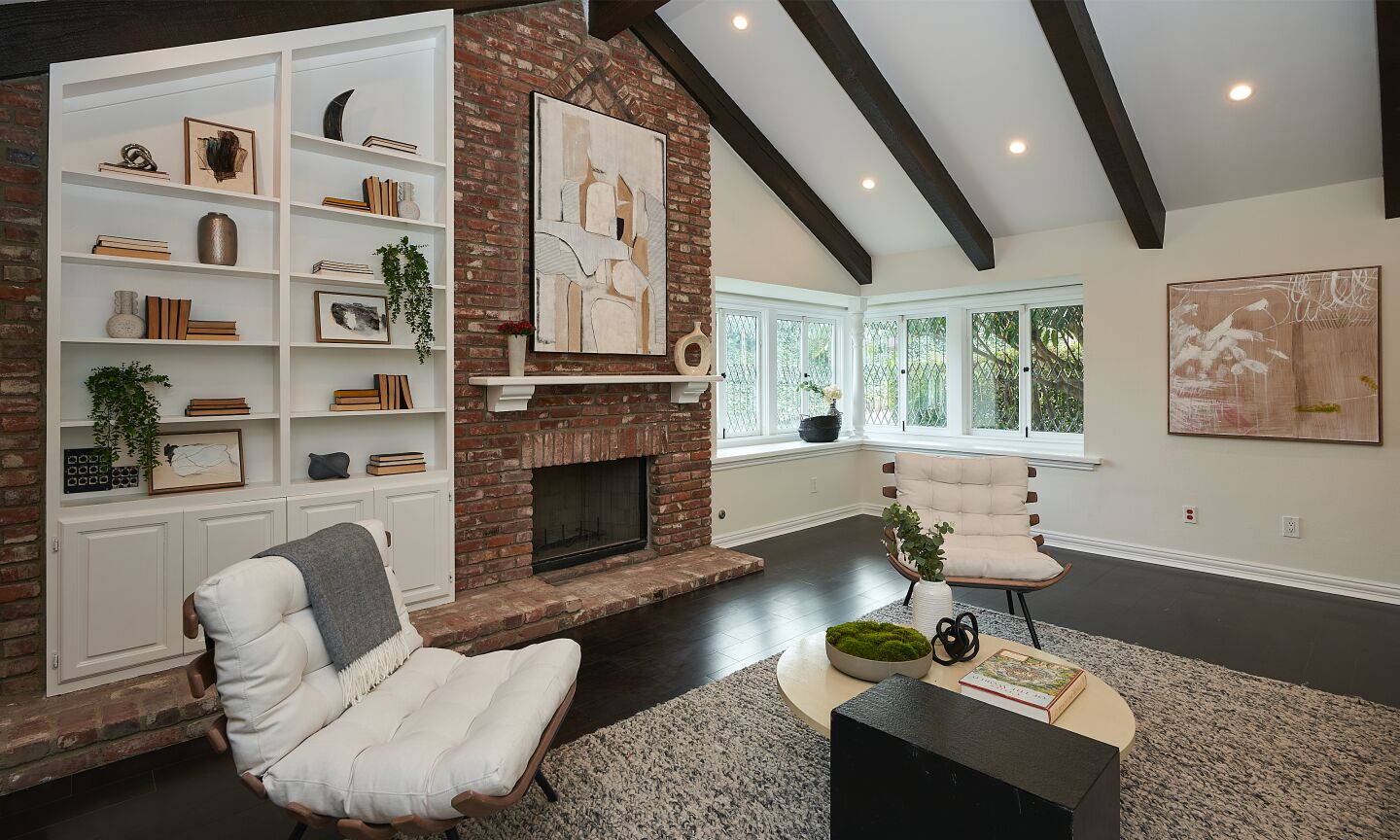A brick fireplace, with white mantelpiece, alongside tall, shallow built-in shelves and wood beamed ceiling.