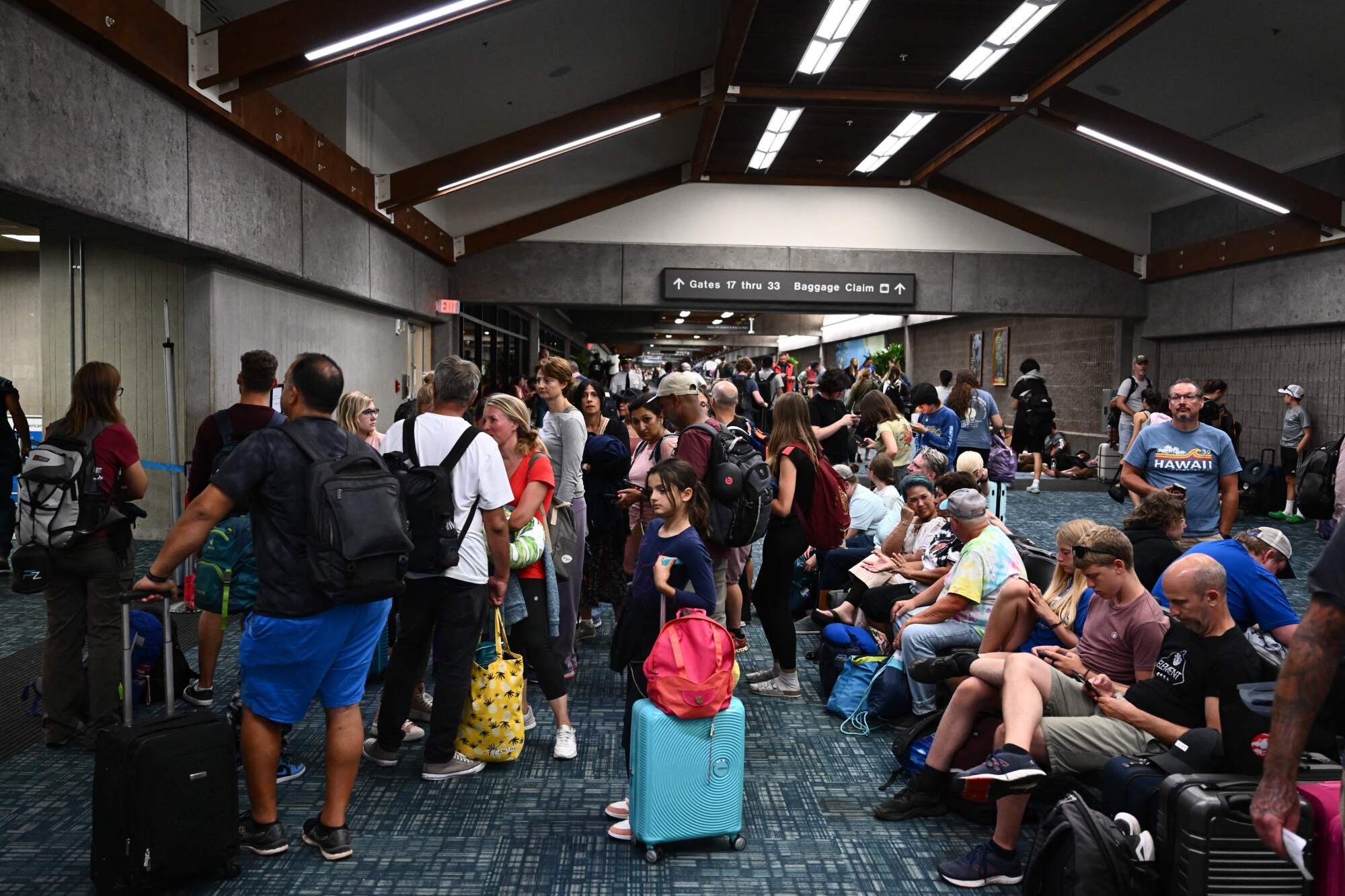 A crowd of people, some seated, with luggage inside an airport 