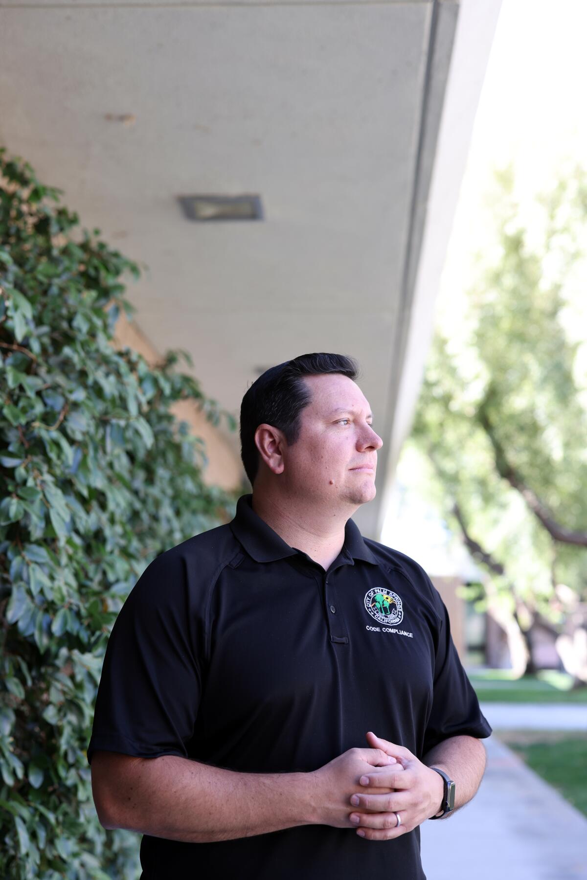 A man stands while wearing a black shirt with a logo on it. 