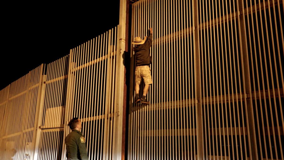 Eduardo Olmos, 38, U.S. Border Patrol agent, apprehends a Mexican man trying to climb the secondary fence into Border Field State Park, San Diego, from Playas de Tijuana,