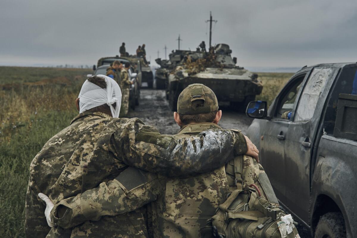 A Ukrainian soldier leans on another as they walk down a road lined with troops in vehicles