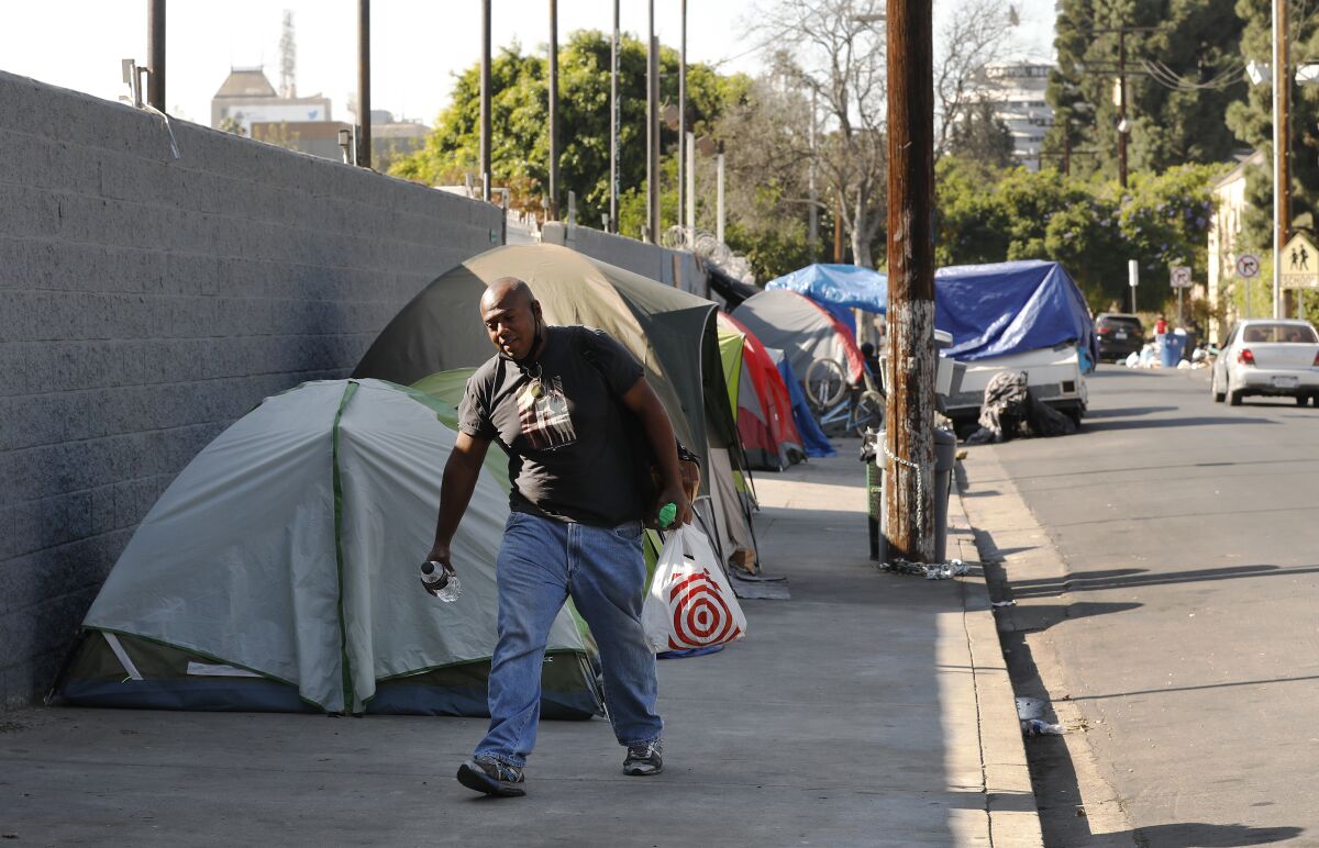 A man walks along a sidewalk lined by tents.