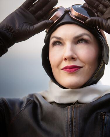 A woman pilot holds onto her goggles on the top of her head 
