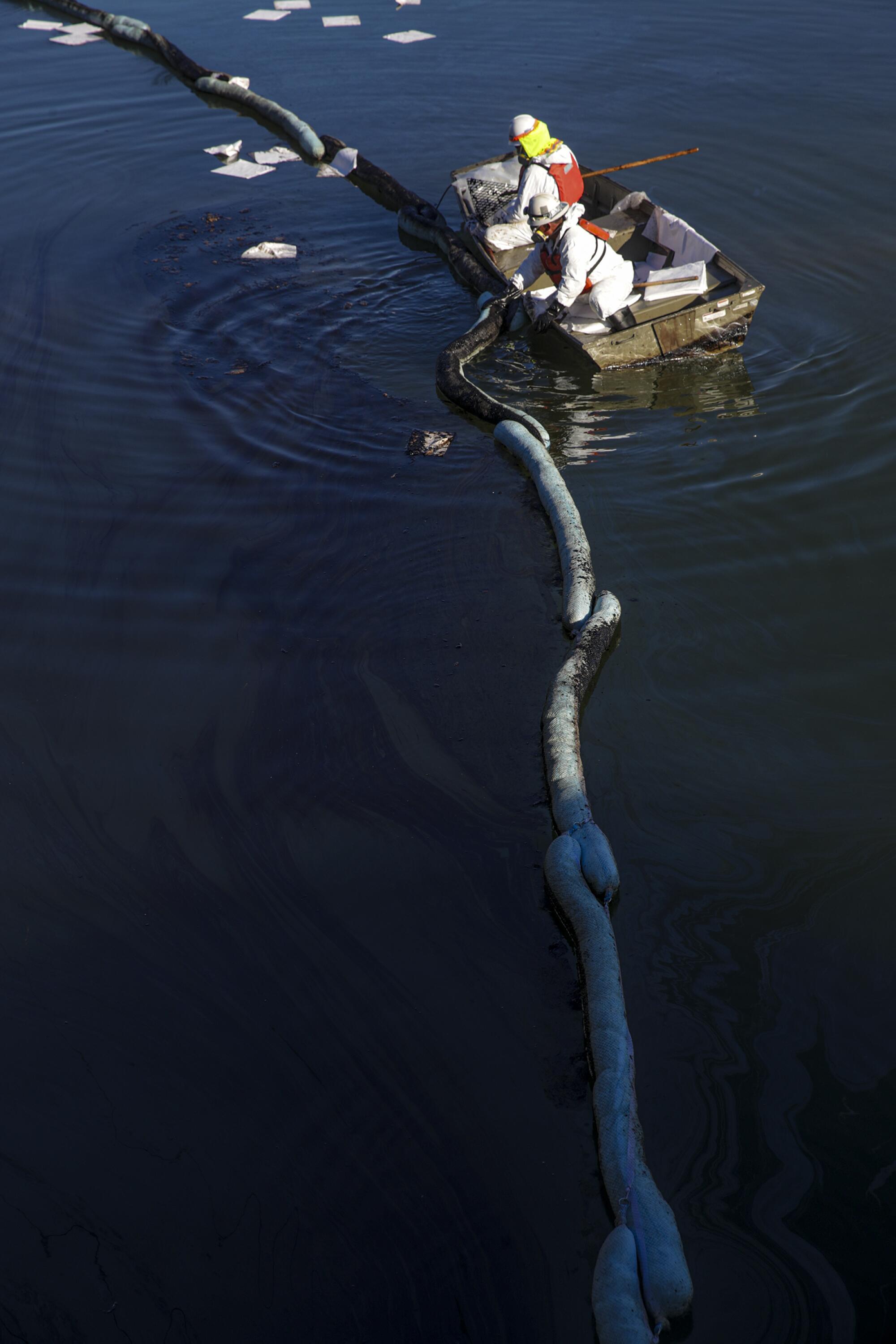 Two workers in a boat near a line of booms in the water 