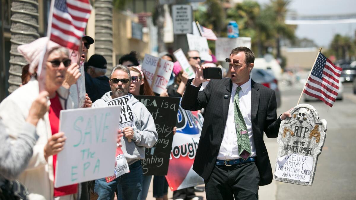 Alex Mathews takes video of protesters outside Rep. Dana Rohrabacher's office in Huntington Beach on Tuesday.