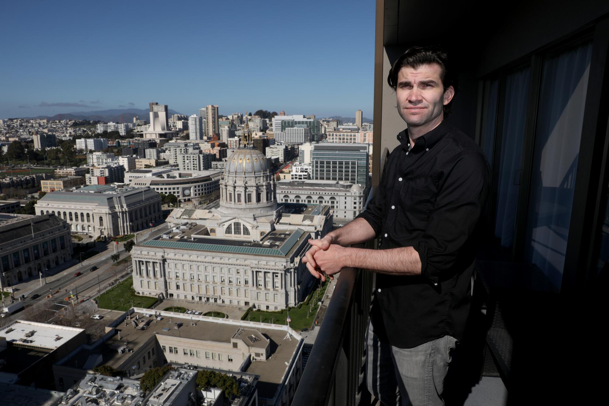Scott Simmons at his one bedroom apartment balcony overlooking City Hall and other buildings in San Francisco