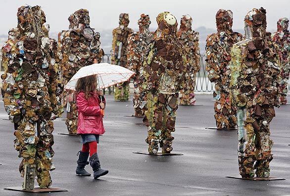 A girl walks past sculptures by German artist H.A. Schuldt titled "Trash People," installed before a meeting in Sicily, Italy, of environment ministers from G-8 nations.