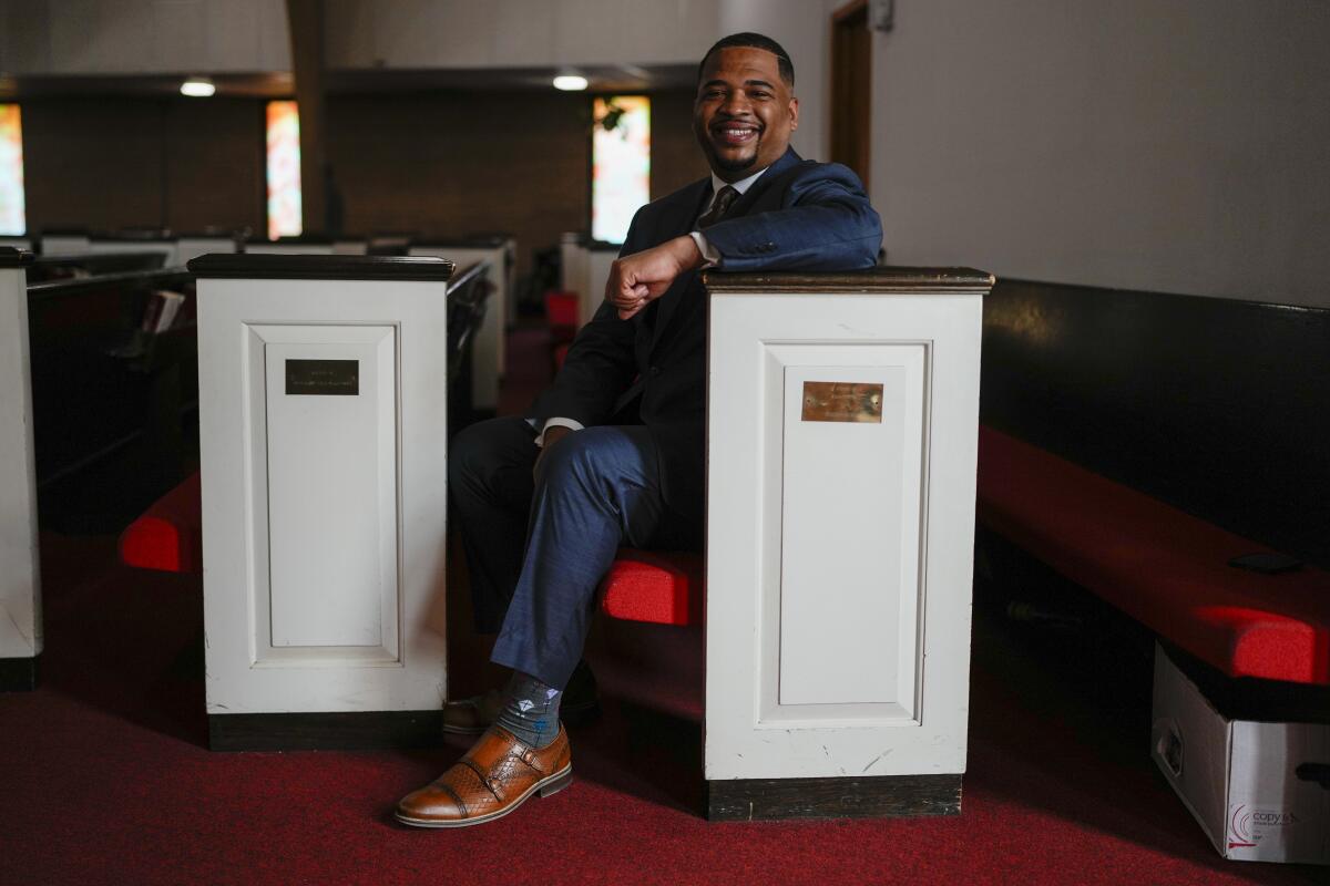 A man in a suit sitting at one end of a white church pew, his arm propped up