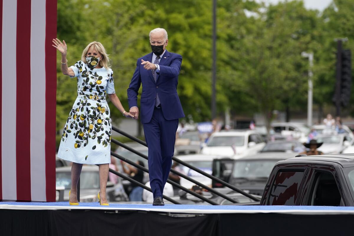 President Biden and First Lady Jill Biden walk onto an outdoor stage holding hands.