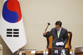 A man bangs a gavel near the South Korean flag.