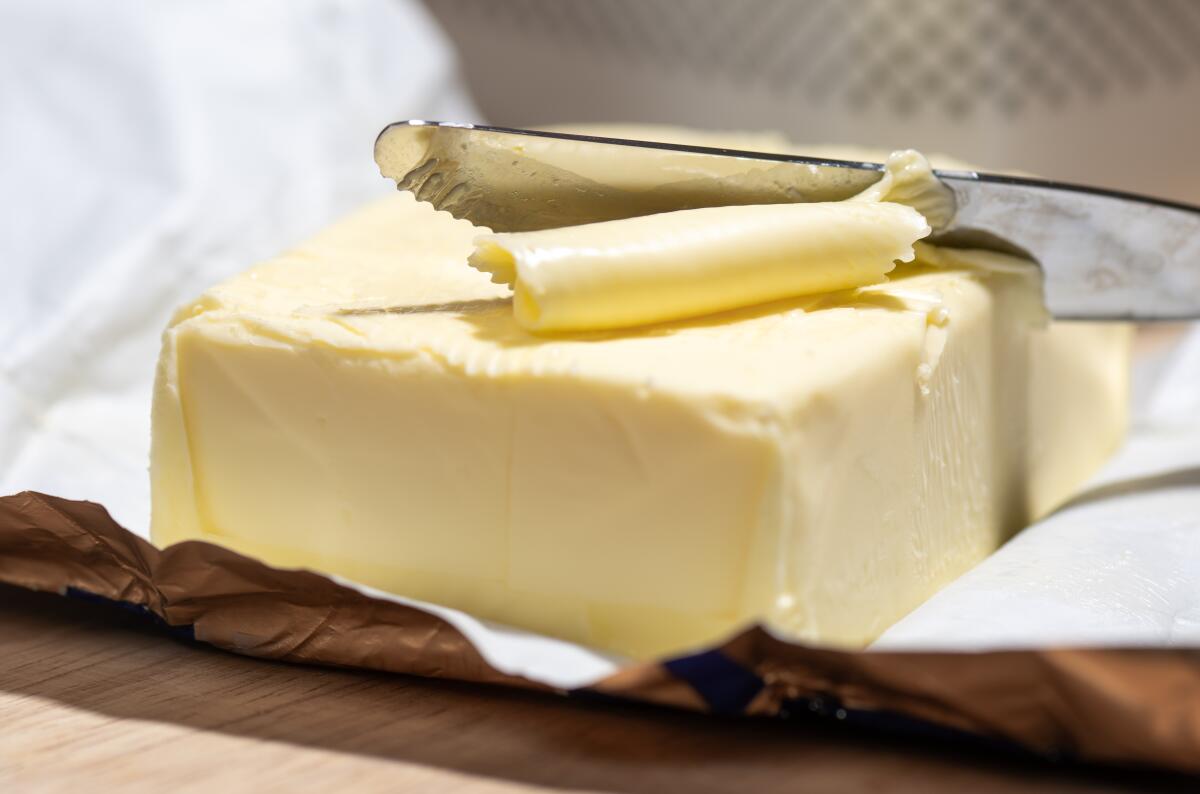  A piece of butter on a foil wrapper with a knife cutting into it